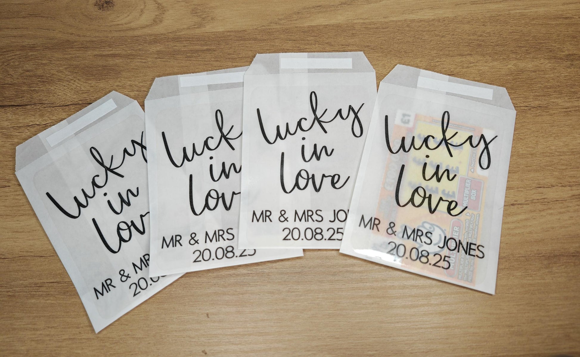 Three glassine bags with 'Lucky in Love' text and personalized details, designed for holding scratch cards for wedding favours.